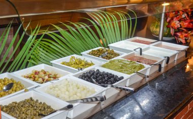 Açık büfedeki konteynırlarda zeytin, sos ve sebze çeşitleri, oteldeki yemek konsepti..