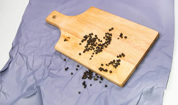 Ervilhas de pimenta preta em uma placa de corte de madeira, vista superior, especiarias — Fotografia de Stock
