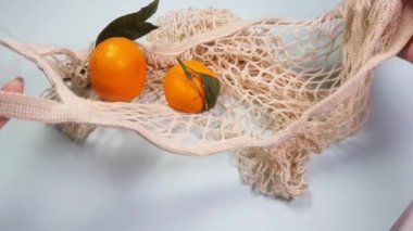 Yeşil yapraklı mandalinalar yeniden kullanılabilir beyaz bir besin torbasına konur. Doğa koruma, ürün yeniden kullanımı ve geri dönüşüm konsepti, sıfır atık konsepti, çevre dostu, makul tüketim, 4K video