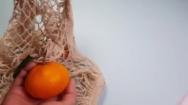Eller tekrar kullanılabilir beyaz bir yemek poşetinden mandalina çıkarır. Şebeke hücreleri, ürün geri dönüşüm konsepti, sıfır atık konsepti, çevre dostu, makul tüketim, 4K video