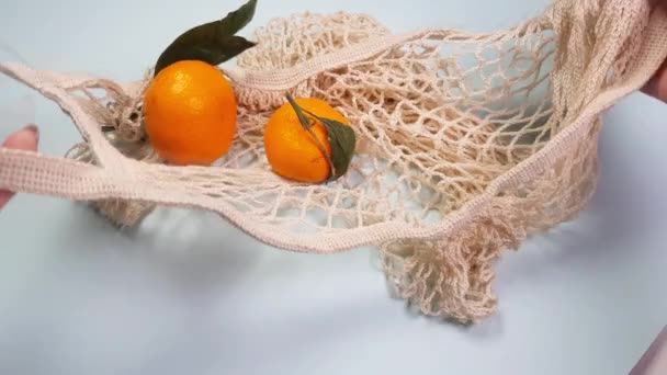 Yeşil yapraklı mandalinalar yeniden kullanılabilir beyaz bir besin torbasına konur. Doğa koruma, ürün yeniden kullanımı ve geri dönüşüm konsepti, sıfır atık konsepti, çevre dostu, makul tüketim, 4K video — Stok video