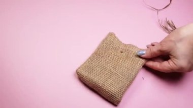 Çiçekçinin elleri kuru otlar ve bir kanvas çantasının üzerinde pembe bir arka plan, DIY konsepti, 4K video.
