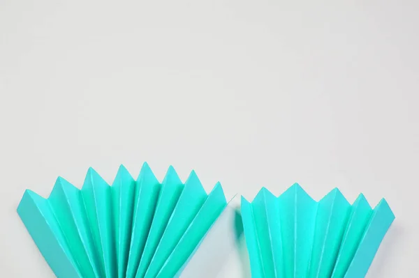 Two light blue origami paper fans located on the bottom edge on a white background, a copy of the space.