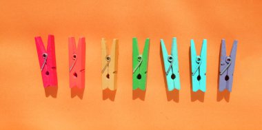 Ruh halini canlandıran renk konsepti, turuncu kağıt arka planda üst üste çok renkli ahşap mandallar. Yaratıcı minimalist tasarım, düz düzen.