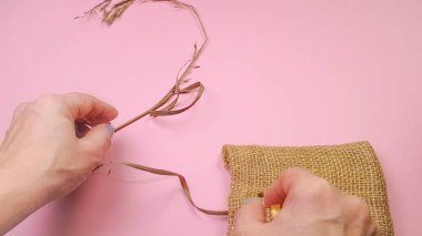 Çiçekçi elleri, kompozisyon için kuru ot ve bez poşet hazırlar, pembe arka plan, DIY konsepti.