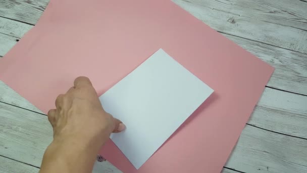 Les mains des femmes ouvrent l'enveloppe blanche et sortent une carte de Saint-Valentin en forme de cœur rouge pour la fête de la Saint-Valentin. Fond rose, déclaration romantique d'amour — Video