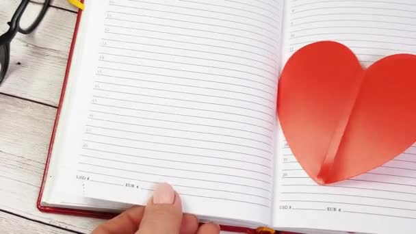 Womens hands flip through the pages of the diary and take out two red hearts, a reminder of the Valentines Day holiday — Stock Video