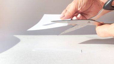 Bir kadının eli, beyaz bir kağıdı makasla keser ve köşeleri keser. Yakın çekim, DIY konsepti