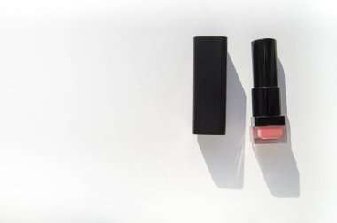 Beyaz arka planda, parlak güneş ışığı ve sert gölgesi olan siyah bir ruj tüpü, güzellik konsepti..