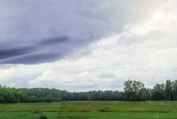 Dramatic storm scene with gray clouds in the field, sunlight breaking through the clouds.