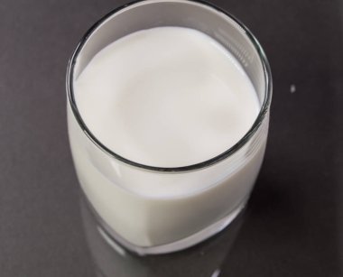 Siyah arka planda cam bardaktaki süt, masadaki camın yansıması..