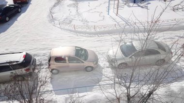 Park yerindeki çok katlı bir binanın penceresinden, sokağa park edilmiş, güneşli bir kış günü..