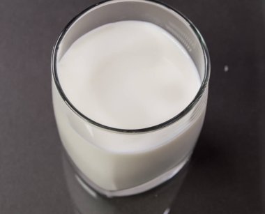 Siyah arka planda cam bardaktaki süt, masadaki camın yansıması..