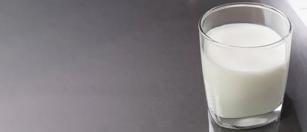 Selective focus top view of a clear glass of milk against the background of a black marble table with a copy space, on the left. Format of the dairy product banner.