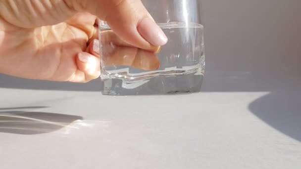 白い背景に冷たい水の透明なガラスの遅い手の回転のクローズアップ — ストック動画