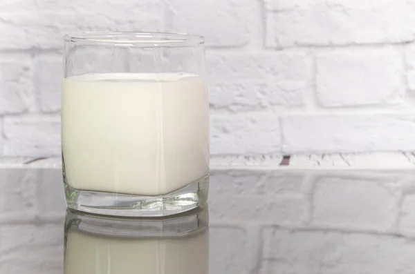 牛奶放在桌上一个透明的玻璃杯里 倒映在一面白色的砖墙后面 — 图库照片