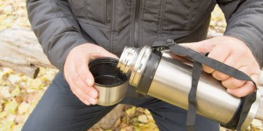 Bir adam sonbahar ormanında ya da parkta oturur ve termostan bir fincana çay döker, yakın plan..