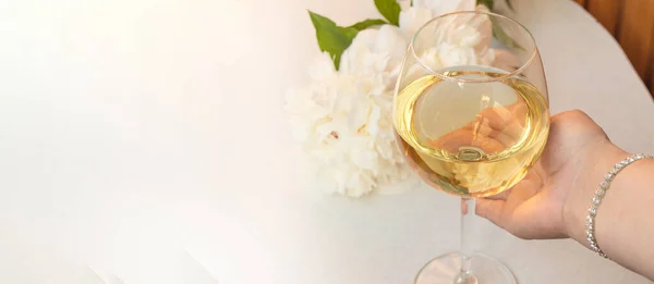 一个女人拿着一杯白葡萄酒 背景是一个白色精致的牡丹 一面横幅 左边是一块空白的复制品 — 图库照片
