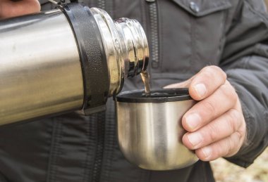 Bir adam sonbahar ormanında ya da parkta oturur ve termostan bir fincana çay döker, yakın plan..