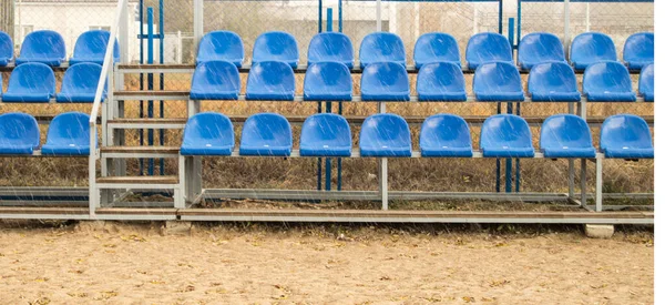 Blue seats on an empty grandstand in an outdoor beach volleyball stadium.