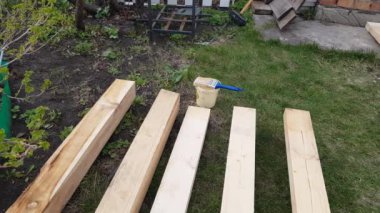 Ahşap kalaslar, keresteler, çimlerin üzerinde duran sanayi odunları. Kırsal kesimdeki bir evin yapımına hazırlanan ahşap kalasları boyamaya hazırlanan bir adamın ayakları..