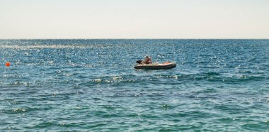 Motoru olan kusurlu bir lastik bot, motoru çalıştıran bir adam, sakin bir denizde bir yaz günü.