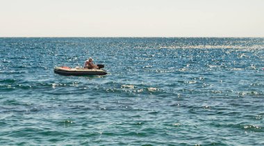 A faulty rubber boat with a motor, a man turns on the motor, a summer day on a calm sea clipart