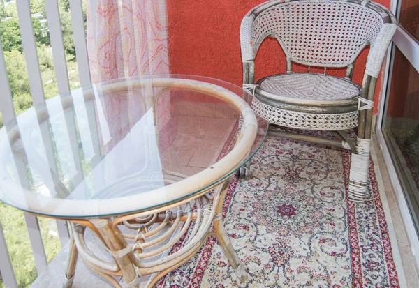 Una cómoda zona de estar en el balcón con una silla de mimbre de ratán, una mesa de vidrio transparente y una alfombra, un concepto de recreación para el hogar — Foto de Stock