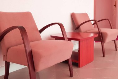 İki pembe koltuk ve aralarında pembe bir duvara dayalı bir sehpa, bir oturma odasının modern bir iç mekanı veya bir otel lobisi..