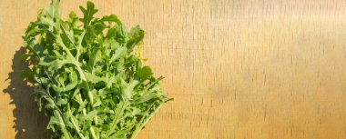 Hafif ahşap zemin üzerinde bir demet taze yeşil roka, parlak güneş ışığı ve gölgeler, üst manzara, düz döşeme, pankart.