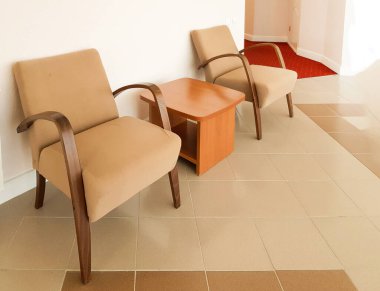 İki kahverengi koltuk ve aralarında pembe bir duvara dayalı bir sehpa. Modern bir oturma odası ya da bir otelin salonu..