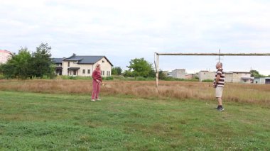 Eski futbol kalelerinin yakınındaki bir sahada badminton oynayan iki kişi, açık havada eğlencenin tadını çıkarıyorlar..