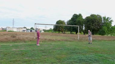 Eski futbol kalelerinin yakınındaki bir sahada badminton oynayan iki kişi, açık havada eğlencenin tadını çıkarıyorlar..