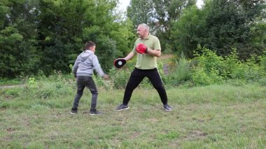 Çocuk, Green Park 'ta yetişkin koçuyla boks antrenmanı yapıyor..