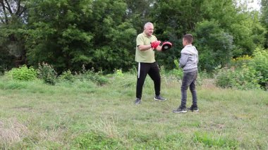 Çocuk, Green Park 'ta yetişkin koçuyla boks antrenmanı yapıyor..
