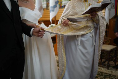 Gelin ve damat, kilisenin düğün ritüeli sırasında kutsama ve ruhsal birlikteliği simgeleyen mezar taşının kenarını tutarlar..      