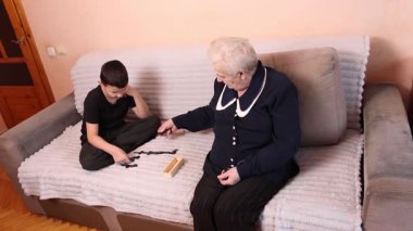 Oğlan ve büyükanne hamlelerini yapmadan önce dikkatlice fayanslarına bakarak domino oynarlar..