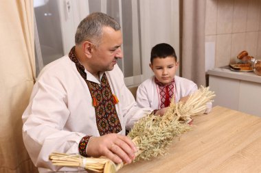 İşlemeli gömlekler içindeki baba ve oğul, zenginliğin sembolü olan buğday saplarından yapılmış didukh 'u inceleyin..