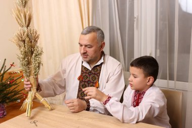 İşlemeli gömlekler içindeki baba ve oğul, zenginliğin sembolü olan buğday saplarından yapılmış didukh 'u inceleyin..