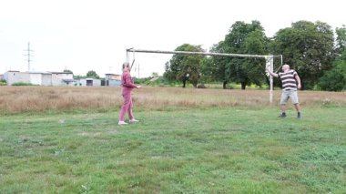 Eski futbol kalelerinin yakınındaki bir sahada badminton oynayan iki kişi, açık havada eğlencenin tadını çıkarıyorlar..