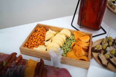 Aperatiflerle dolu ahşap kutu: cips, fındık, yeşil wasabi topları, içki servisi..                    