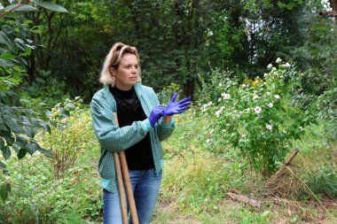 Bahçede işe hazırlanan bir kadın omzunda çapayla koruyucu eldiven takıyor..