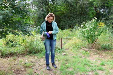 Bahçede işe hazırlanan bir kadın omzunda çapayla koruyucu eldiven takıyor..