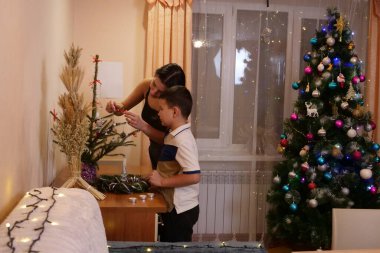 Bir çocuk ve ablası evde küçük bir Noel ağacı süsleyerek şenlik ayrıntılarını ekliyor ve aile sıcaklığını vurguluyorlar..