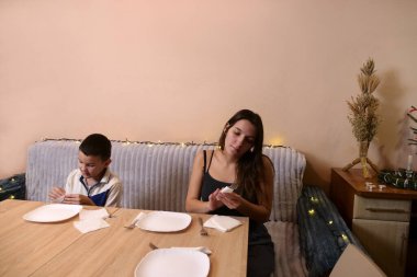 Erkek ve kız kardeş Noel ağacının olduğu bir odaya sofra, tabak, çatal bıçak takımı ve peçeteler kurdular. Ilık ışıklandırma ve yumuşak odaklanma sıcak bir aile ortamı yaratır..