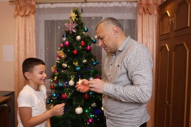 Baba ve oğul yılbaşını ya da yılbaşını kutlamak için Noel ağacının yanında havai fişek yakıyor..