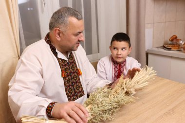 İşlemeli gömlekler içindeki baba ve oğul, zenginliğin sembolü olan buğday saplarından yapılmış didukh 'u inceleyin..