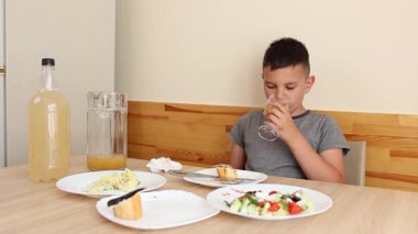 Çocuk masada oturuyor, lezzetli yemekler yiyor ve meyve suyu içiyor..