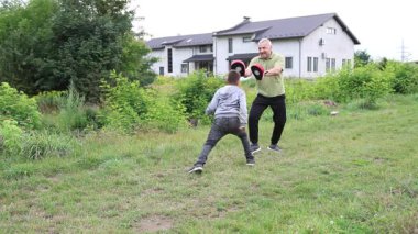 Çocuk, Green Park 'ta yetişkin koçuyla boks antrenmanı yapıyor..