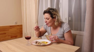 Bir kadın sebzeli fırında tavuk yer ve şarap içer..